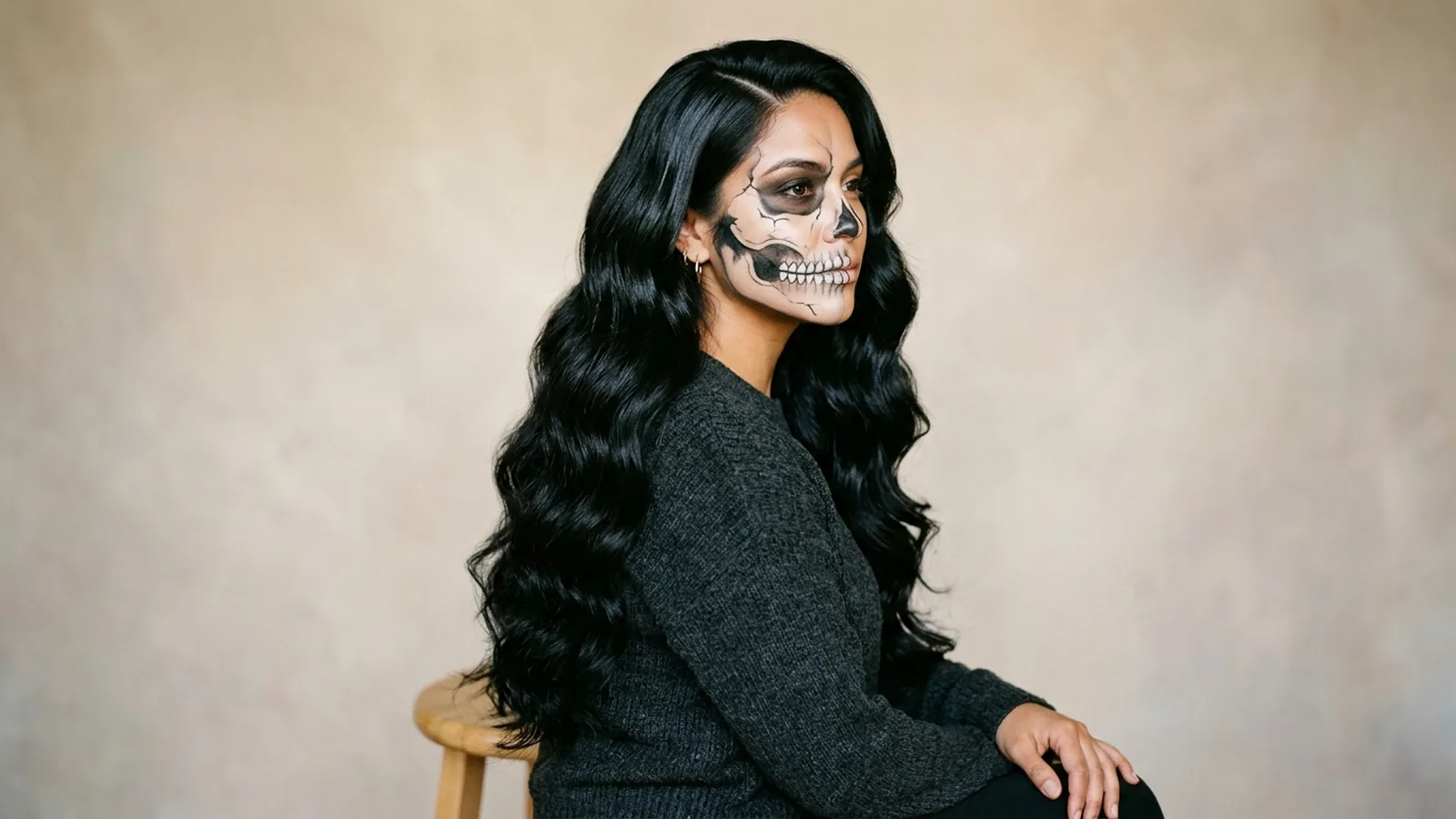 Woman with waist-length wavy black hair swept over one shoulder wearing half-face sugar skull makeup